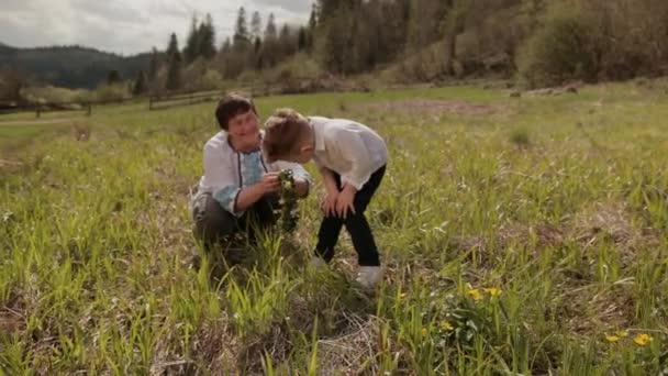 Großmutter macht mit ihrem kleinen Enkel einen Kranz aus Wildblumen. Draußen entspannen — Stockvideo