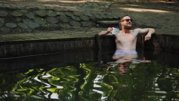 Está na hora de relaxar. Jovem barbudo com óculos de sol nu torso sentado na natação — Vídeo de Stock