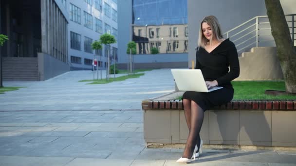 Mujer atenta trabajando en un banco sentado portátil en la calle. Empresaria — Vídeos de Stock