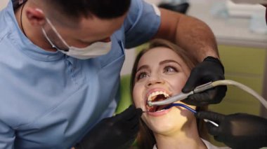 Diş hekimi asistanı, diş teçhizatı, diş sağlığı. Diş tedavisi sırasında, gülümseyen hasta birden fazla araç kullanan dişçi ve asistan tarafından tedavi edilir..