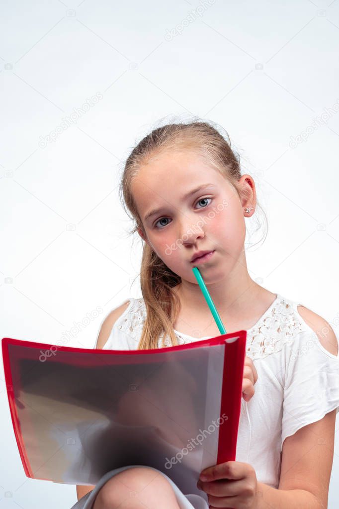 A cute 10-year-old caucasian schoolgirl looking a bit worried while holding a pencil against her chin and a note pad on her knees