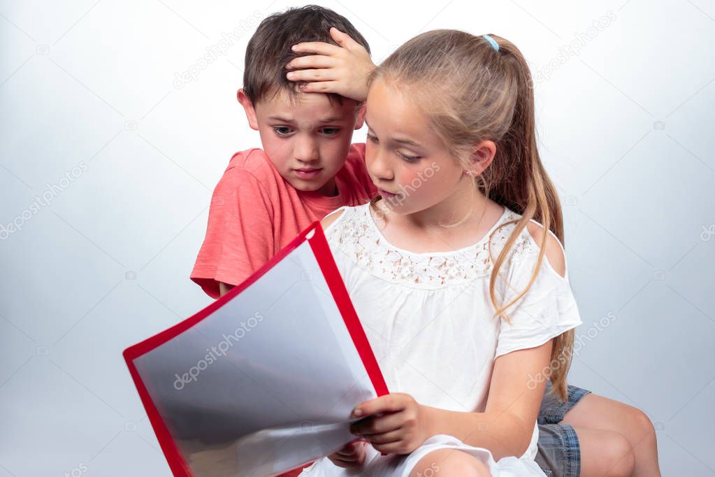 Caucasian schoolchildren studying, a cute girl holding notes, explains a boy who looks confused and strikes his hand in his hair on light background. Education concept