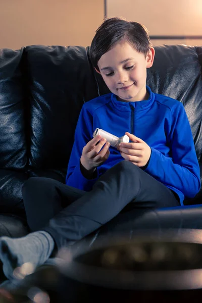 8 year old boy wearing sportive clothing holding an asthma inhaler sitting in sofa. Concepts : health, illness, doping