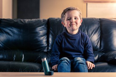 Siyah deri kanepe otururken kameraya bakarak astım inhaler ile şirin 5 yaşındaki yürümeye başlayan çocuk