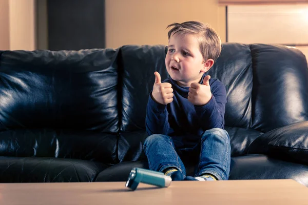 可爱的5岁幼儿与哮喘吸入器竖起大拇指从镜头外 而坐在黑色真皮沙发 — 图库照片