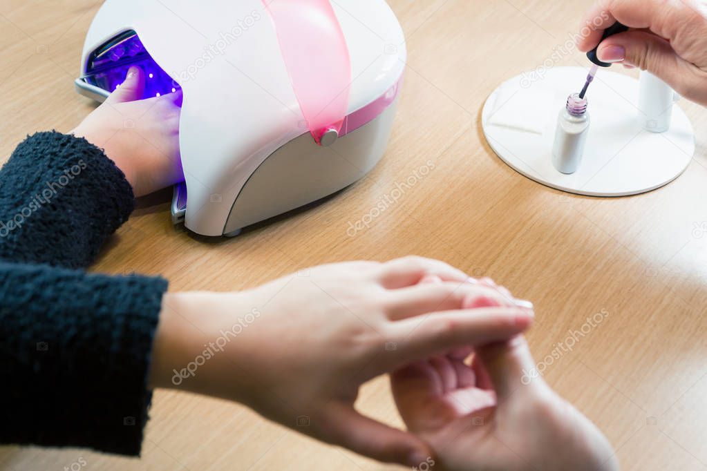 Hand holding other hand while applying nail polish - dry nail polish with UV lamp