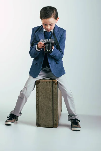 Young boy in suit with camera sitting on suitcase