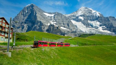 Kleine Scheidegg, Bernese Oberland, İsviçre - Ağustos 12019: Jungfraujoch 'dan (Avrupa' nın tepesi) taze yeşil çayırlarda gelen kırmızı tren. Arka planda Eiger kuzey cephesi ve monch
