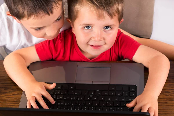 4歳の幼児はラップトップコンピュータで楽しみ カメラを見て 兄は肩越しに見ています 白い背景に隔離された高い角度の眺め — ストック写真