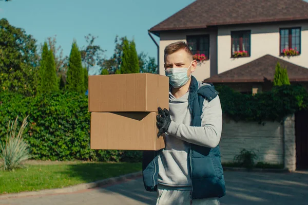 Delivery man with two boxes stands outside the house and looks at the camera
