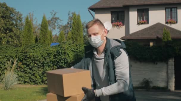 Egy férfi egy ház mellett orvosi maszkban jelenik meg a keretben két dobozzal. — Stock videók