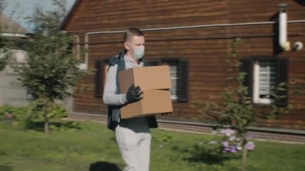 คนส่งของในหน้ากากป้องกันและถุงมือเข้าใกล้บ้าน — วีดีโอสต็อก