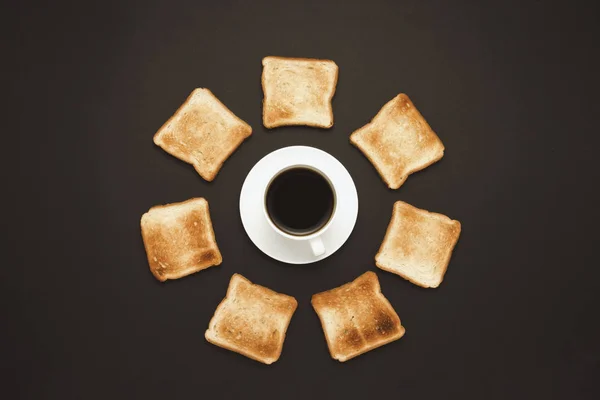 White cup with coffee and Toast piled around on a dark background. Flat lay, top view.