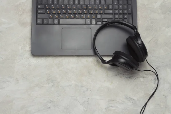 Black Laptop and Black Headphones on a Light Stone Background. Flat lay, top view.
