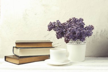 Leylak beyaz dekoratif kova, kitap yığını, kahve beyaz taş zemin üzerine beyaz Kupası.