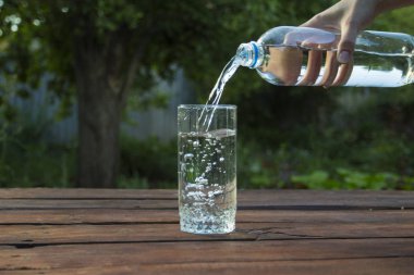 El bir bahar bahçe ahşap bir masa üzerinde bir bardak içine bir plastik şişe su dökülen.