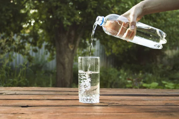 El bir bahar bahçe ahşap bir masa üzerinde bir bardak içine bir plastik şişe su dökülen.