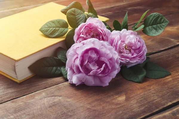 Pink roses and book with a yellow cover on a wooden background. The concept of books about love and novels.