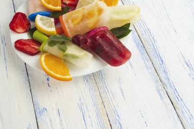 Renkli, ev yapımı meyve buzlu şeker, taze meyve beyaz tabak hafif ahşap arka plan üzerinde. Çilek, limon, nane limon, portakal, vişne, karışık.