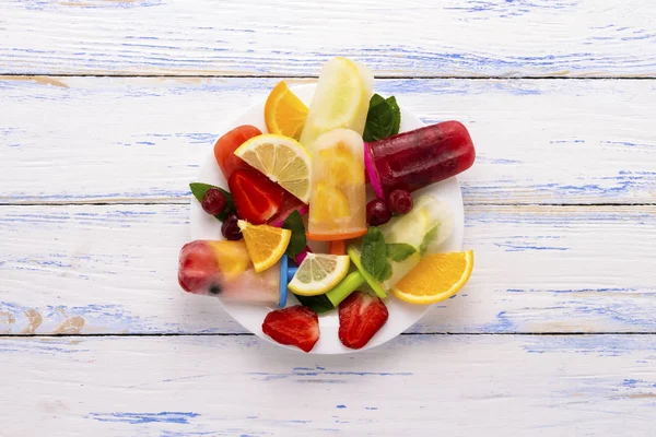 Homemade colorful, fruit popsicle, Fresh fruit on a white plate light wooden background. Strawberry, Lemon, Lemon with mint, Orange, Cherry, Multifruit. Flat lay, top view.