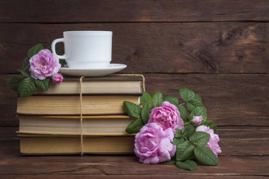 Kitaplar, beyaz fincan kahve ve koyu ahşap arka plan üzerinde pembe bir gül yığını.
