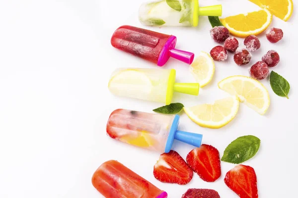 Homemade Multicolored bright fruit popsicle with strawberry, cherry, lemon, orange, lemon and mint and slices of fresh fruit on a light white background. Flat lay, top view.