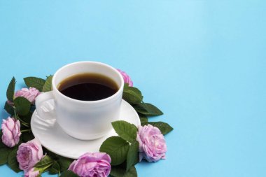 Beyaz fincan etrafında çizgili mavi bir arka plan üzerinde siyah kahve ve pembe güller.