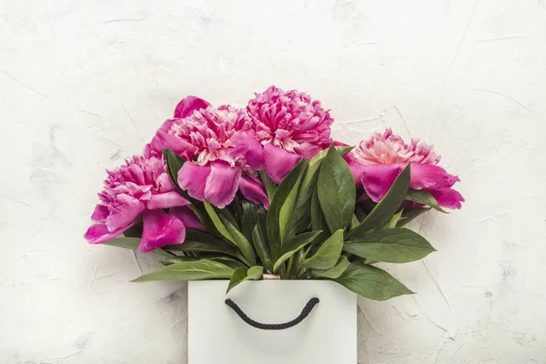 Bouquet of peonies in paper bag on white texture
