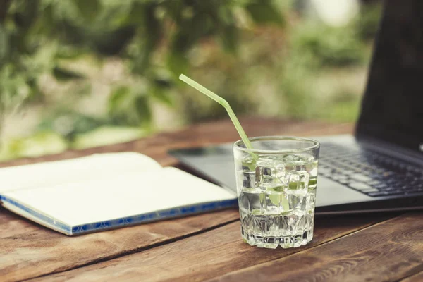 Laptop, açık günlüğü ve bir bardak buz küpleri ve nane ile ferahlatıcı bir içki ile ahşap bir masaya bırakır. Doğada, freelancing, tatilde iş iş kavramı.