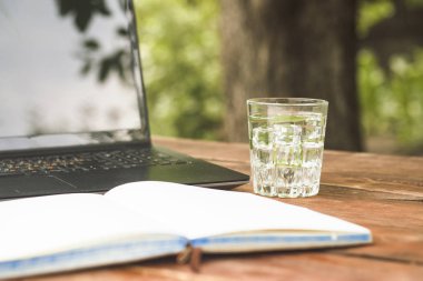 Laptop, açık günlüğü ve bir bardak buz küpleri ve nane ile ferahlatıcı bir içki ile ahşap bir masaya bırakır. Doğada, freelancing, tatilde iş iş kavramı.