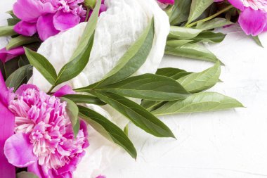 Pembe peonies hafif bir taş zemin üzerine pembe bir kurdele ile beyaz bir kumaş sarılmış.