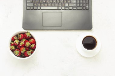 Çalışma alanı. Dizüstü bilgisayar, bir fincan kahve, bir kase çilek. Üstten görünüm, düz yatıyordu