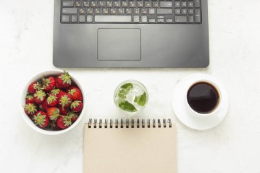 Çalışma alanı. Laptop, defter, fincan kahve, bir kase çilek ve serinletici bir içecek buz ve nane ile. Üstten görünüm, düz yatıyordu