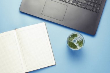 Çalışma alanı ile Laptop, buz ve nane, mavi bir arka plan üzerine açık bir günlük taze bir içkiyle. Bir gazeteci, yazar, çevirmen, metin yazarı, çalışma alanı kavramı.