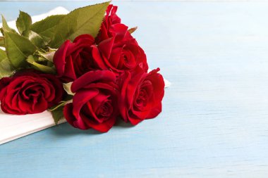 Bir beyaz peçete ve mavi ahşap arka plan üzerinde kırmızı gül buketi. Uzay kopyalayın. Sevgililer günü tatil için romantik hediye.