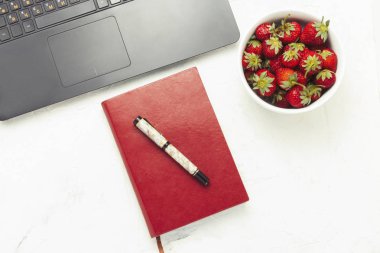 Dizüstü bilgisayar, günlük ve beyaz bir ışık taş zemin üzerine çilek plakalı. İş yerinde kahvaltı kavramı. Düz yatıyordu, en iyi görünümü.