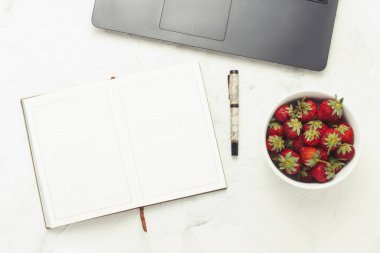 Dizüstü bilgisayar, günlük ve beyaz bir ışık taş zemin üzerine çilek plakalı. Evde rahat bir ortamda çalışma kavramı. Düz yatıyordu, en iyi görünümü.