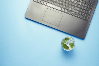 İşyeri dizüstü bilgisayar, buz ve mavi bir arka plan üzerine nane taze içki ile. Bir gazeteci, yazar, çevirmen, metin yazarı, çalışma alanı kavramı. Düz yatıyordu, en iyi görünümü.