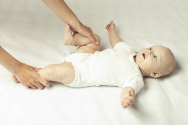 Anne yatakta beyaz bir levha ile küçük bir bebek için günlük Jimnastik yapar. Düz yatıyordu, en iyi görünümü.