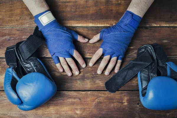 Men\'s hands in boxing bandages and boxing gloves on a wooden background. Concept preparation for boxing training or combat. Flat lay, top view.