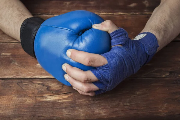 man's hand in boxing bandages holds a hand in a boxing glove on a wooden background. Ready gesture. The concept of training for boxing training or fighting. Flat lay, top view.