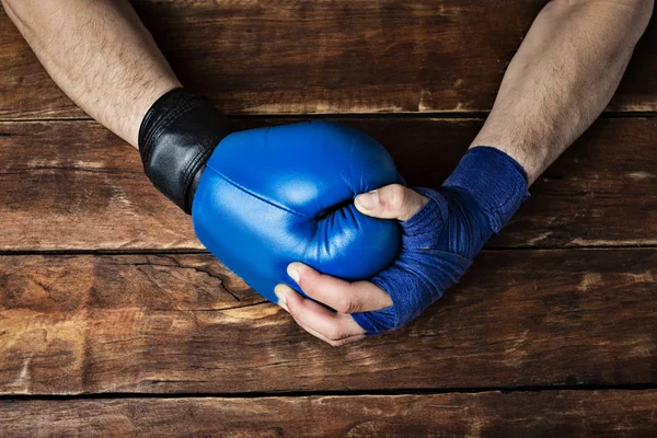 man's hand in boxing bandages holds a hand in a boxing glove on a wooden background. Ready gesture. The concept of training for boxing training or fighting. Flat lay, top view.