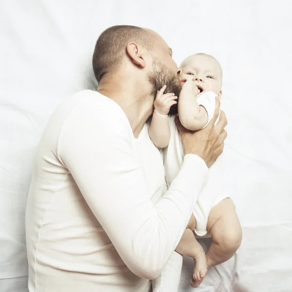 Young dad and little baby in white clothes lay on the bed with white sheets. Flat lay, top view.
