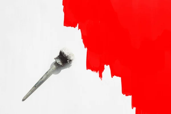 Paint brush in white paint on a wooden background is painted in white and half in red. Flat lay, top view.