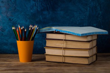 Açık günlük, bir bardak renkli kalemler, kazık kitap bir ahşap masa ve mavi arka plan.