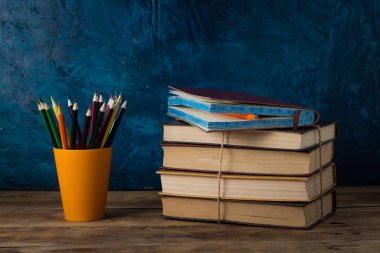 Renkli kalemler bir cam, ahşap bir masa ve mavi bir arka plan üzerinde kitap yığını. Okula dönüş.