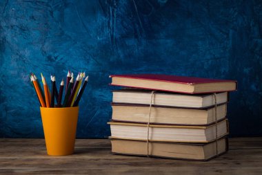 Renkli kalemler bir cam, ahşap bir masa ve mavi bir arka plan üzerinde kitap yığını. Okula dönüş.