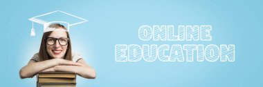Beyaz bir elbise, gözlük ve çizilmiş öğrenci şapka genç kız mavi zemin üzerine kitap yığını ellerini koymak. Eklenen metin Online eğitim. Online eğitim ve uzaktan eğitim kavramı. Afiş.
