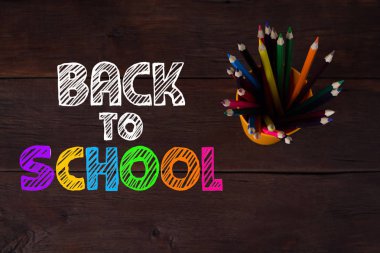 Ahşap arka plan üzerinde renkli kalemler yığını. Okul için eklenen metin.