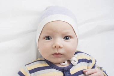 Beyaz çarşafta komik bir yüz ifadesi olan küçük bir bebeğin portresi. Düz yatış, üst görünüm.